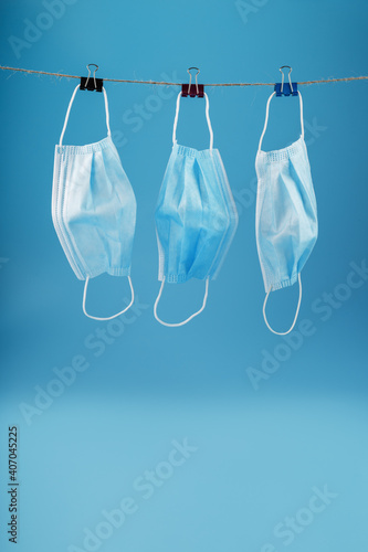 Three surgical masks hang on a clothesline against a blue background.