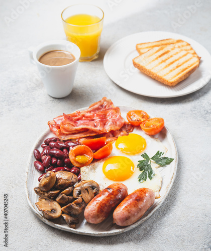 English Breakfast with fried eggs, sausages, bacon, beans, toasts, tomatoes and mushrooms on white plate, concrette background, Top view