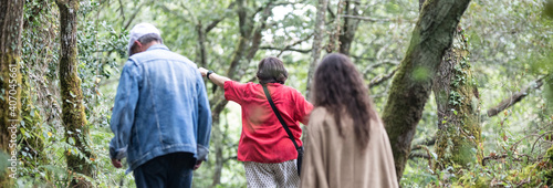 three people walk through the field. Two older and one young. They are seen from behind between the trees
