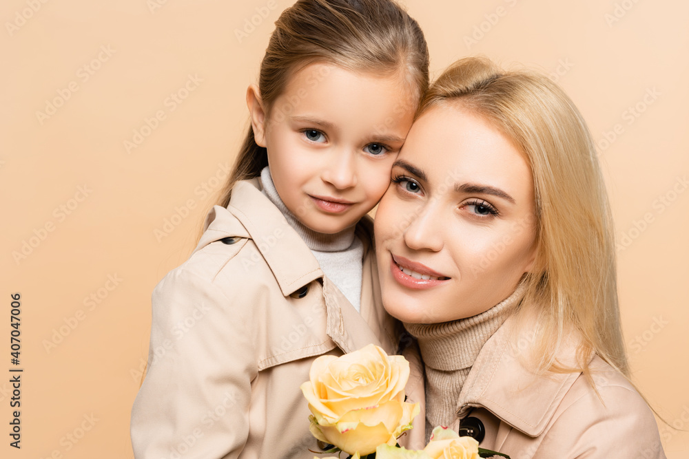 joyful mother holding flowers and hugging daughter isolated on beige joyful mother holding flowers and hugging daughter isolated on beige