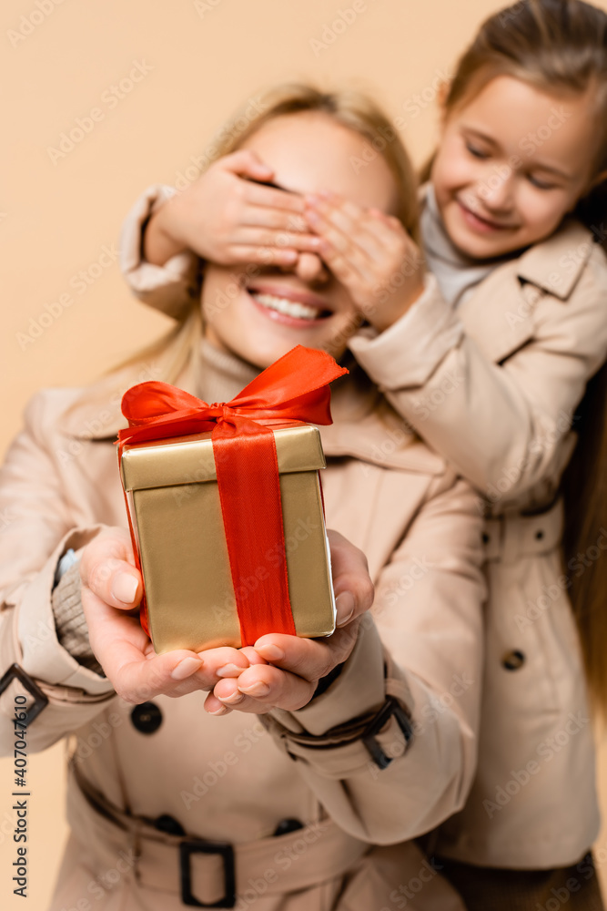 smiling kid covering eyes of happy mother with present isolated on beige smiling kid covering eyes of happy mother with present isolated on beige