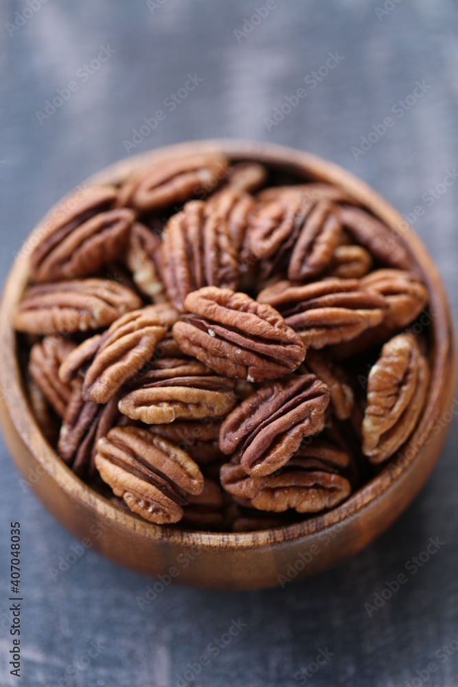 Pecan nut close-up in a round wooden cup on a black shabby board on wooden table background.Nuts and seeds. .Healthy fats.Heap shelled Pecans nut closeup. Pecan nut close-up in a round wooden cup on a black shabby board on wooden table background.Nuts and seeds. .Healthy fats.Heap shelled Pecans nut closeup.