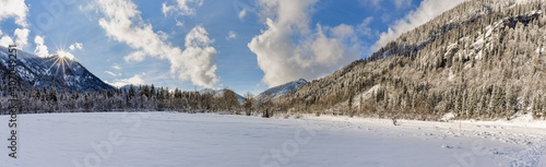 Gefrorener See in den Bergen, bei Sonne une Wolken im Winter mit Schnee