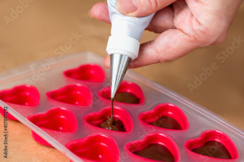 Handmade valentines day dessert. Making chocolate candy, Female hands filling heart shaped mold from pastry bag