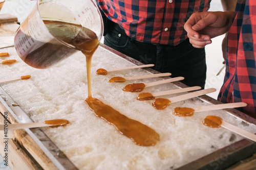 Tablou pe pânză Two man pouring maple syrup on ice to prepare lollipops