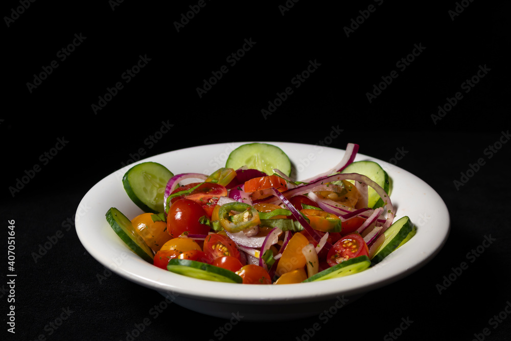 Fresh two-color cherry tomato salad, cucumber, red onion and hot chili served in a vintage bowl on a table. 45 deg. view.Black background.