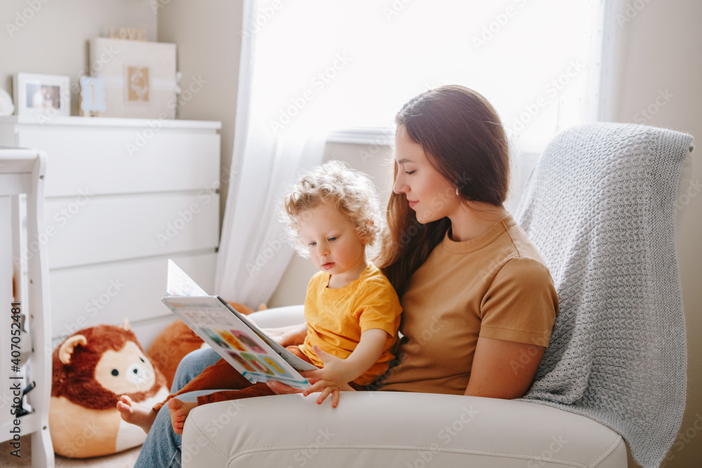Mom reading book with baby boy toddler at home. Early age children education, development. Mother and child kid spending time together. Family authentic candid lifestyle. - obrazy, fototapety, plakaty 
