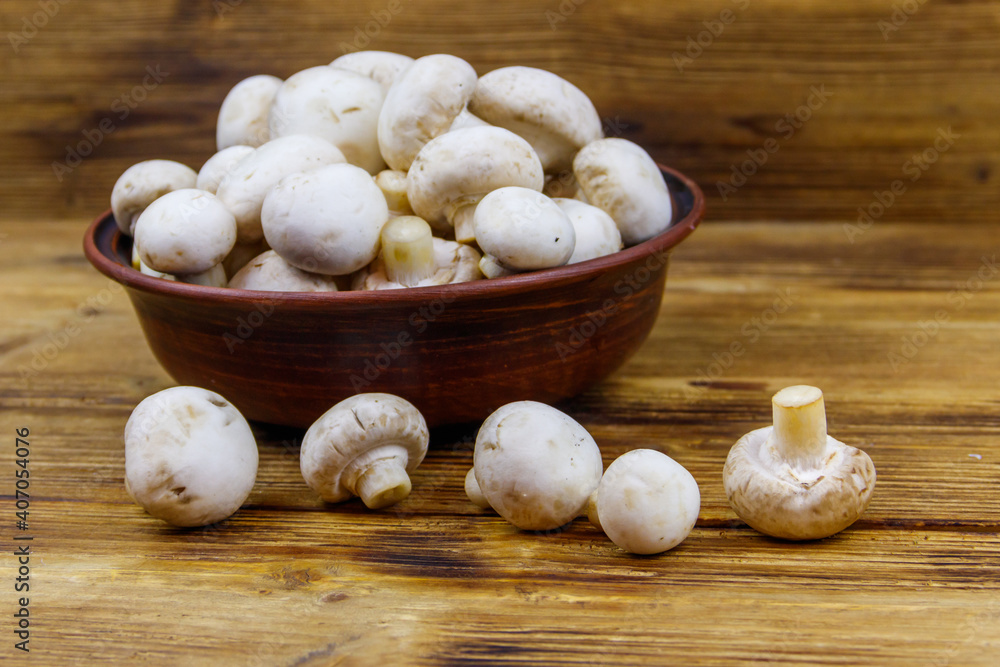 Fresh champignon mushrooms in ceramic bowl on the wooden table Fresh champignon mushrooms in ceramic bowl on the wooden table