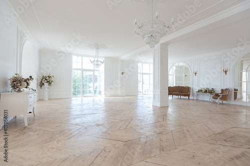 chic white huge spacious hall with a minimum of expensive antique furniture. Baroque interior design with ornament on the walls and parquet on the floor.