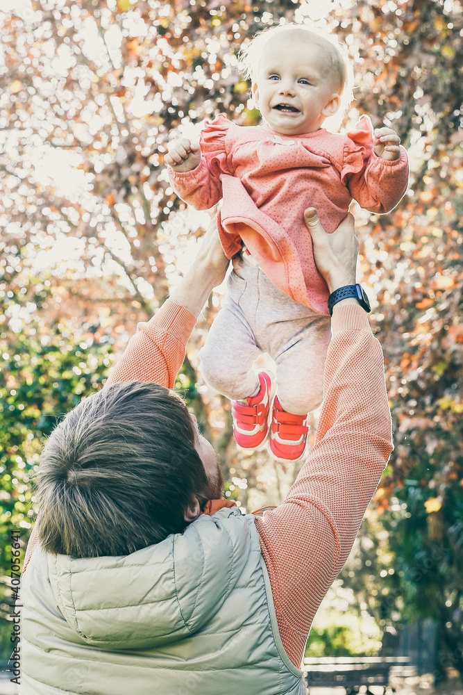 Dad lifting happy excited baby daughter in air, playing with kid outdoors. Vertical shot. Family and childhood concept