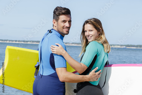 couple in wetsuits looking back towards camera