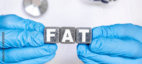 FAT - word from stone blocks with letters holding by a doctor's hands in medical protective gloves