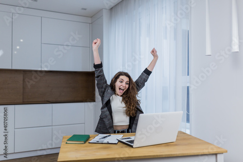 Work complete. Young, woman, specialist rejoicing her finished work with raised fists sitting at her desk