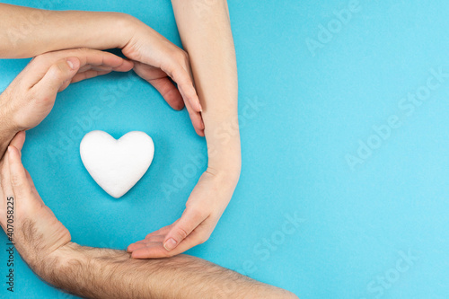 Fototapeta Naklejka Na Ścianę i Meble -  Hands of parents and a child surround a white heart on a blue background. Family concept, flat lay, top view