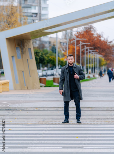 Handsome man on street background. Crossing the street face to the camera. Dark gray coat on.