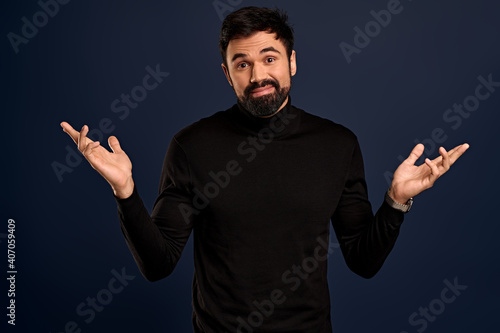 Carefree, indecisive young handsome businessman in black high neck sweater, shrugging raise hands sideways, tilt head and smiling as apoligizing, cant help, not know answer, standing Blue background