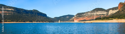 Panoramic landscape of the Sau swamp with its church. Tavertet and Collsacabra cliffs in the Sau Reservoir on a sunny day. Tourism in Osona, Barcelona, Catalonia, Spain.