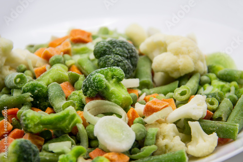 Frozen vegetables: cauliflower, green peas, leeks, broccoli, carrots, green beans on a white plate.