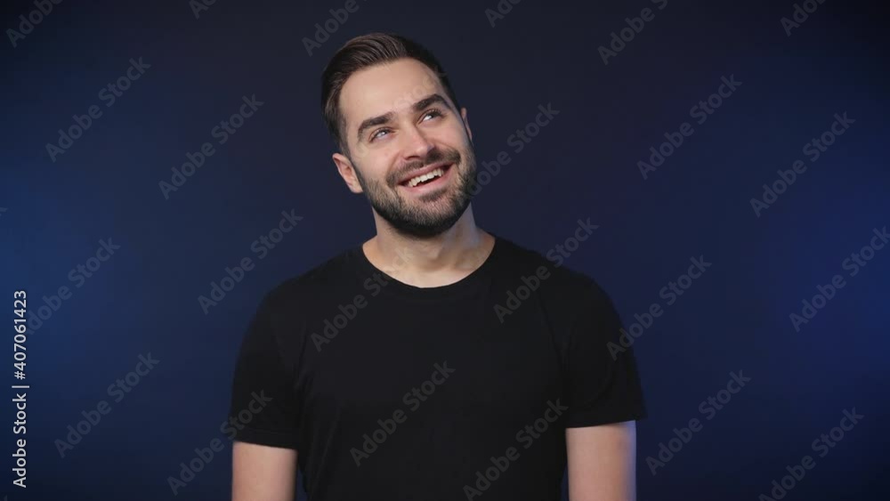 Smiling pensive cheerful bearded young man 20s years old wearing black casual basic t-shirt isolated on dark blue color background studio. People sincere emotions lifestyle concept. Looking aside up Smiling pensive cheerful bearded young man 20s years old wearing black casual basic t-shirt isolated on dark blue color background studio. People sincere emotions lifestyle concept. Looking aside up