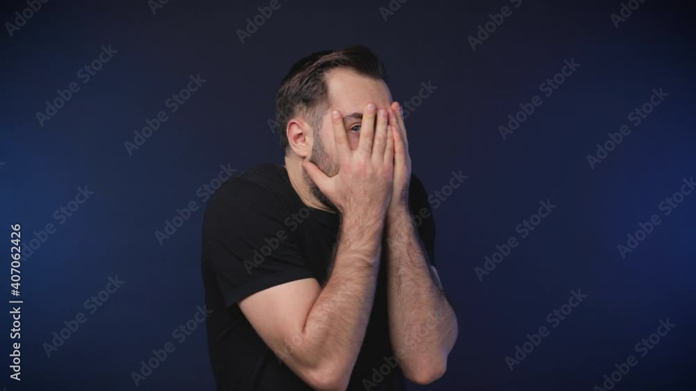 Shocked scared worried bearded young man 20s years old in black casual basic t-shirt isolated on dark blue color background studio. People sincere emotions lifestyle concept. Covering face with hands Shocked scared worried bearded young man 20s years old in black casual basic t-shirt isolated on dark blue color background studio. People sincere emotions lifestyle concept. Covering face with hands