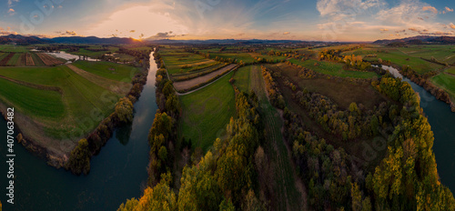 Spectacular aerial panorama of river flowing through fields at sunset.