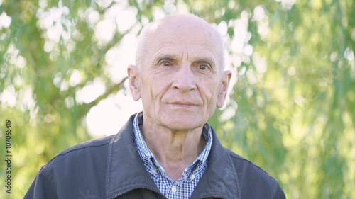 Outdoor video portrait of old gray haired bald man with red sick eye. Concept oldness and disease. photo