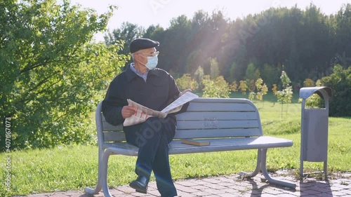 Aged man wearing medical face mask and glasses reading newspaper outdoor. Concept leisure and knowledge. photo