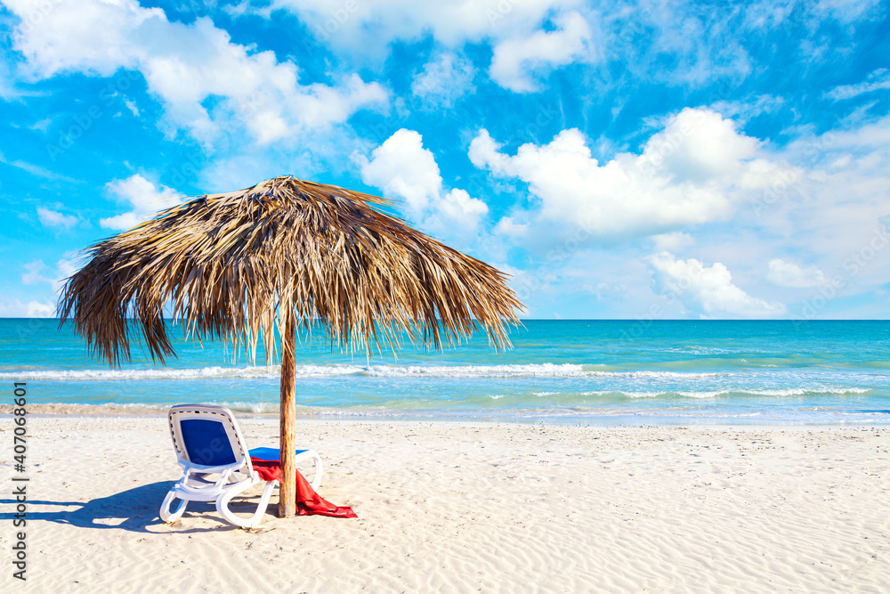 Relaxation and vacation idyllic background. Straw umbrella with sun lounger and red towel on the beach in Varadero, Cuba.