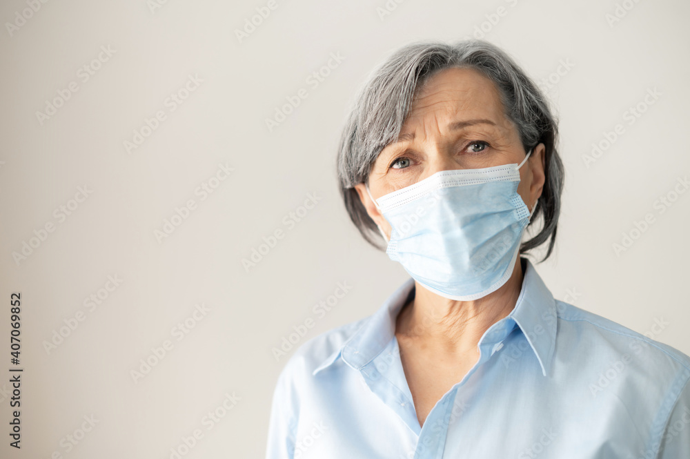 Portrait of a sad senior middle-aged female businesswoman with gray hair wearing a face mask, looking at the camera, headshot of doctor at the workplace, stay safe, stay at home, protect grandparents Portrait of a sad senior middle-aged female businesswoman with gray hair wearing a face mask, looking at the camera, headshot of doctor at the workplace, stay safe, stay at home, protect grandparents