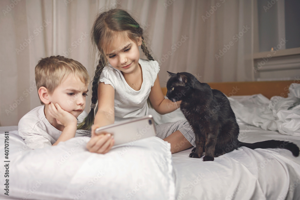 Obraz premium Sleepy kids in pajama watching video on smartphone in bed and struggling to sleep in the evening, healthy sleeping, invest in rest concept