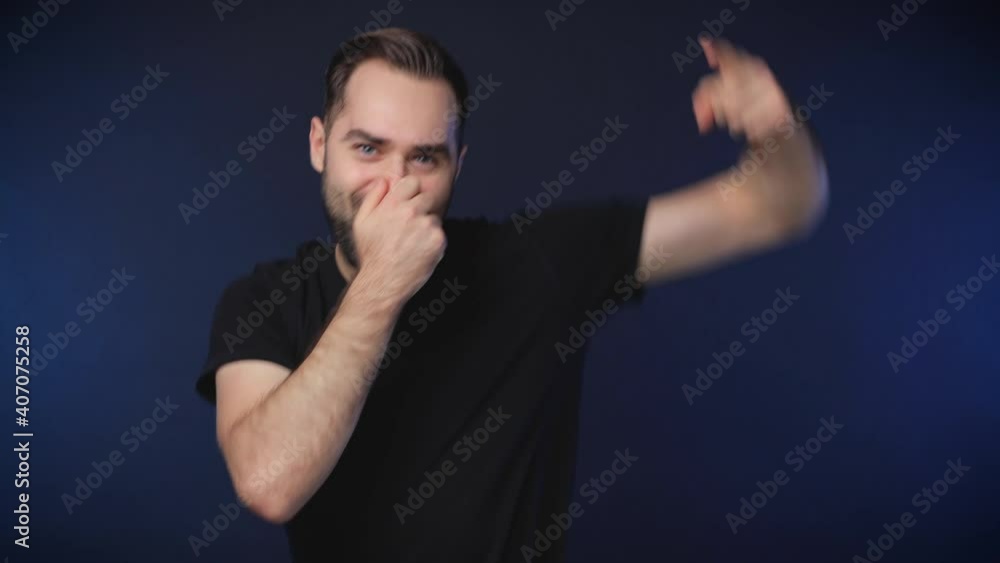 Cheerful bearded young man 20s in black casual t-shirt isolated on dark blue background studio. People lifestyle concept. Dancing showing victory sign put hands on nose clenching fists waving hands Cheerful bearded young man 20s in black casual t-shirt isolated on dark blue background studio. People lifestyle concept. Dancing showing victory sign put hands on nose clenching fists waving hands