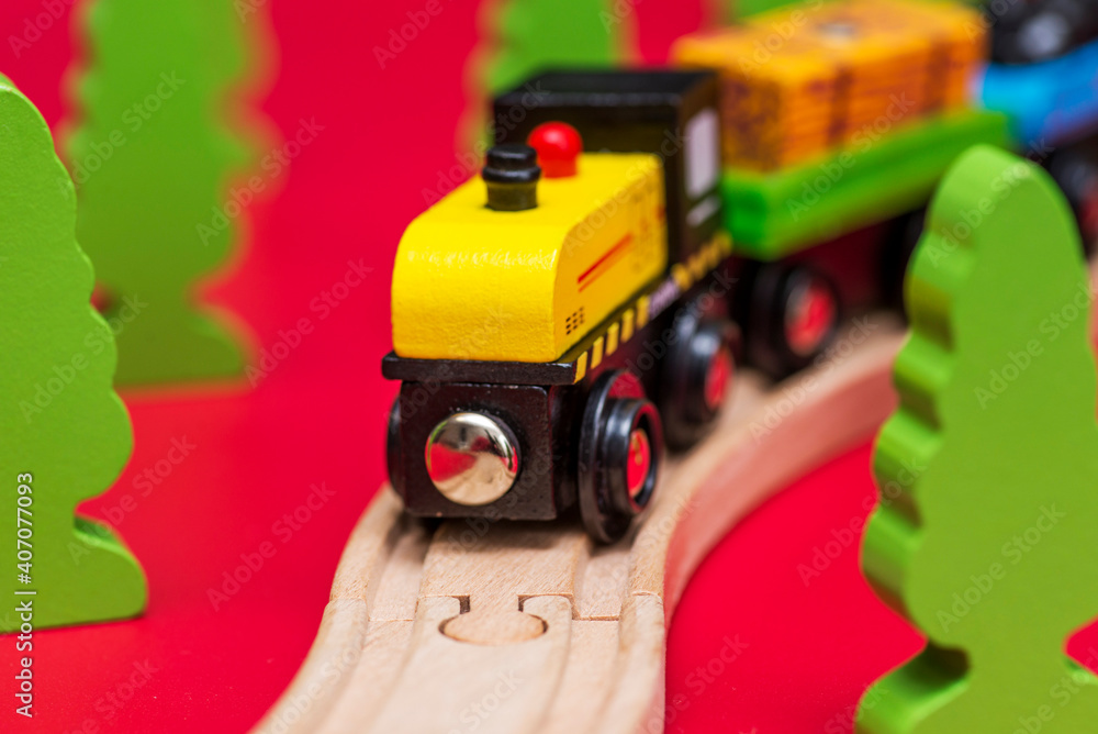 Fototapeta premium Wooden toy train on the railroad among green trees on red background. Educational toys for preschool and kindergarten child