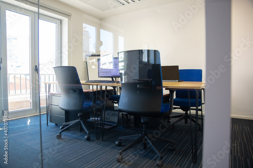 Empty meeting room behind glass wall. Boardroom with meeting table, shared desk for team and workplaces. Office interior or commercial real estate concept