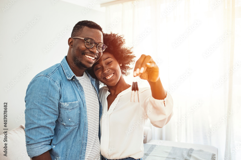 Foto de Young smiling couple showing keys to new home hugging looking ...