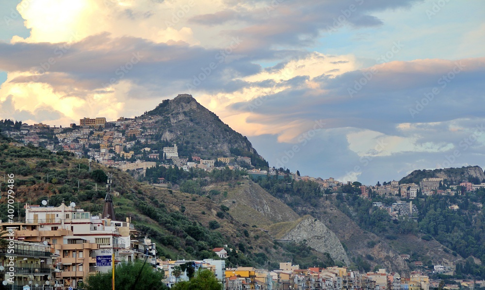 view of a town on a hillside, a town by the sea in Italy, buildings located on hills, light breaking through the clouds