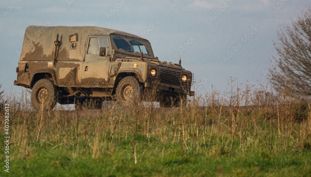 mud covered army land rover defender 4x4 driving along a track