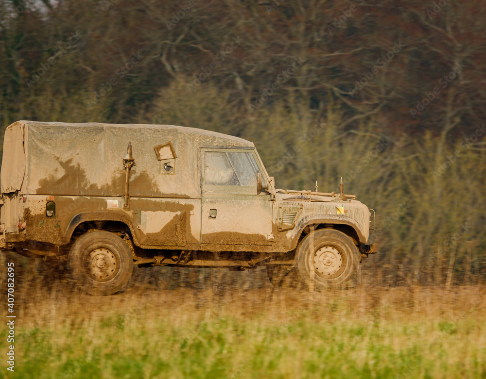 mud covered army land rover defender 4x4 driving along a track