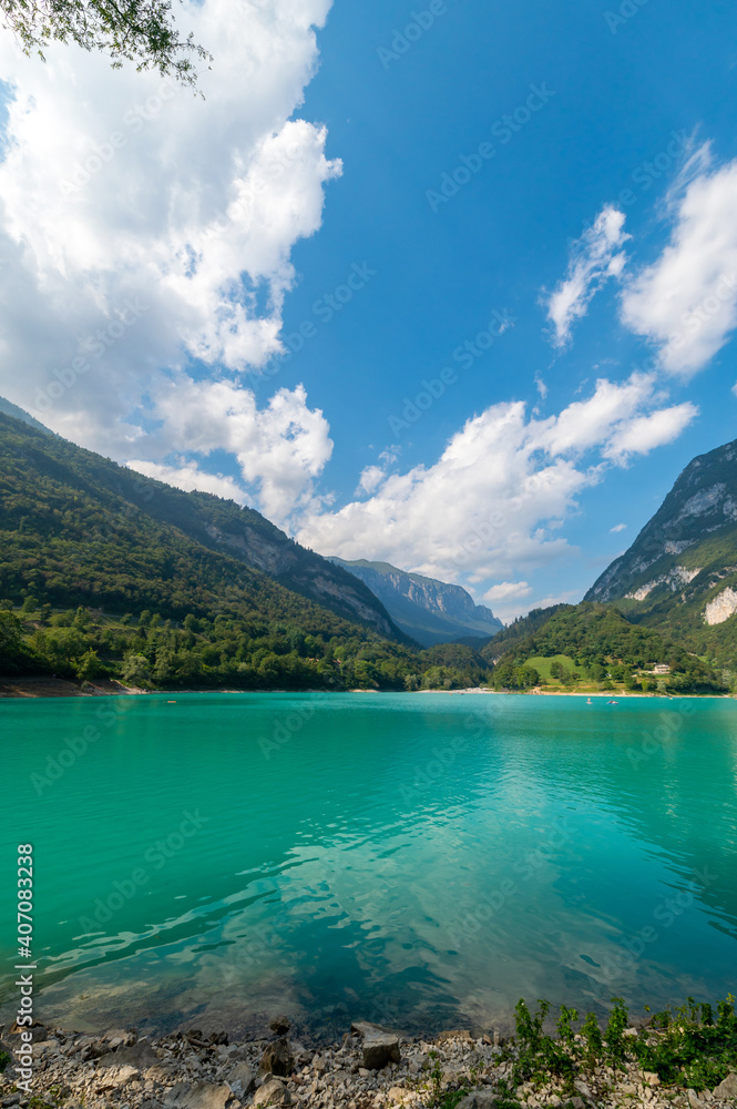 Cavedine Lake. Panorama of the turquoise waters, with the alpine mountains in the distance rich in vegetation. Blue sky and clouds on a summer day. Trentino, Trento