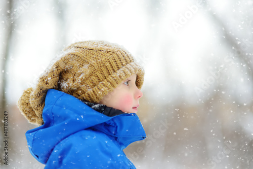 Obraz na plátně Funny little boy with frostbitten cheeks in blue winter clothes walks during a snowfall