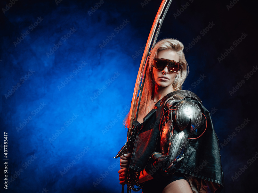 Naklejka premium Gorgeous and seductive female warrior with blond hairs and sword from the future poses in dark background.