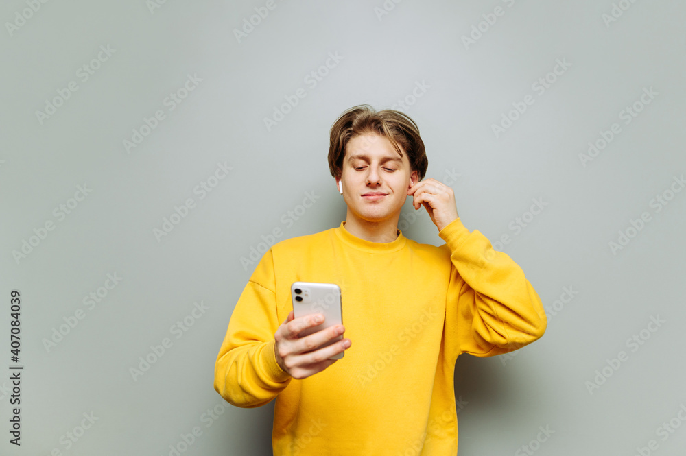 Cheerful guy in yellow clothes uses a smartphone on a gray background and listens to music in headphones with a smile on his face. Cheerful guy in yellow clothes uses a smartphone on a gray background and listens to music in headphones with a smile on his face.