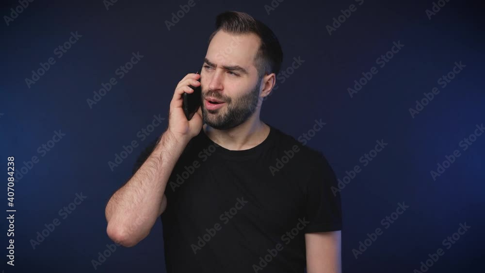 Perplexed angry bearded young man 20s in black casual basic t-shirt isolated on dark blue background studio. People lifestyle concept. Talking on mobile cell phone spreading hands screaming swearing Perplexed angry bearded young man 20s in black casual basic t-shirt isolated on dark blue background studio. People lifestyle concept. Talking on mobile cell phone spreading hands screaming swearing