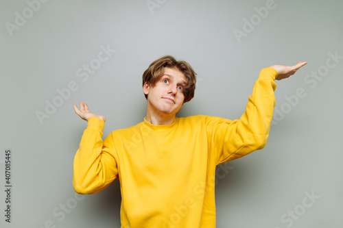 Canvas Print Portrait of puzzled guy in casual clothes on a gray wall background, spreads his arms away from confusion