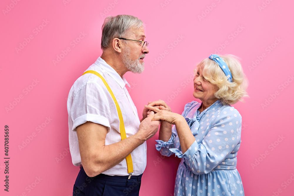 man confesses his feelings to wife isolated on pink background, gray-haired couple in love. man holding woman's hands man confesses his feelings to wife isolated on pink background, gray-haired couple in love. man holding woman's hands