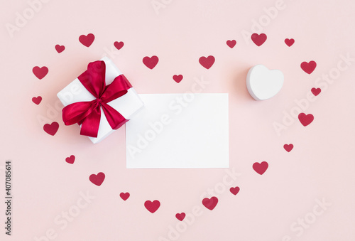 Valentine's day greeting card with blank sheet, gift and paper hearts on pink background. Love concept. Space for text. Top view