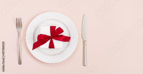 Festive table setting with a gift in a plate on a pink background. Banner. Space for text. Top view. Valentines Day, Mothers Day, Birthday or Christmas.