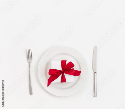 Table setting with a gift box with a red bow in a plate on a white background. Valentines Day, Mothers Day, Birthday or Christmas concept. Copy space, top view, flat lay