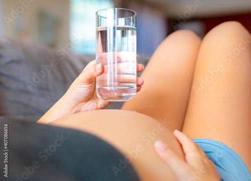 A pregnant woman drinking a glass of water. Prenatal health and hydration.