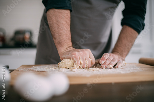 A male chef prepares noodle dough at home in the kitchen. Close up of hands with flour and dough