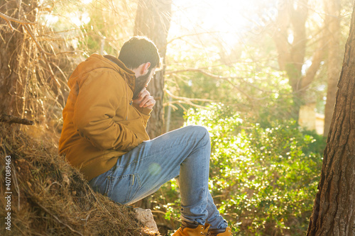 Fototapete Young man sitting in a Mediterranean landscape forest with sun in background and